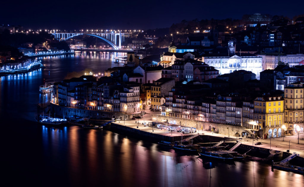 Riverside buildings and a bridge reflected in the water at night